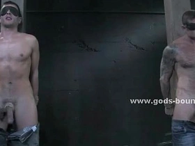 Muscular gay men engage in BDSM activities with bondage and leather equipment.